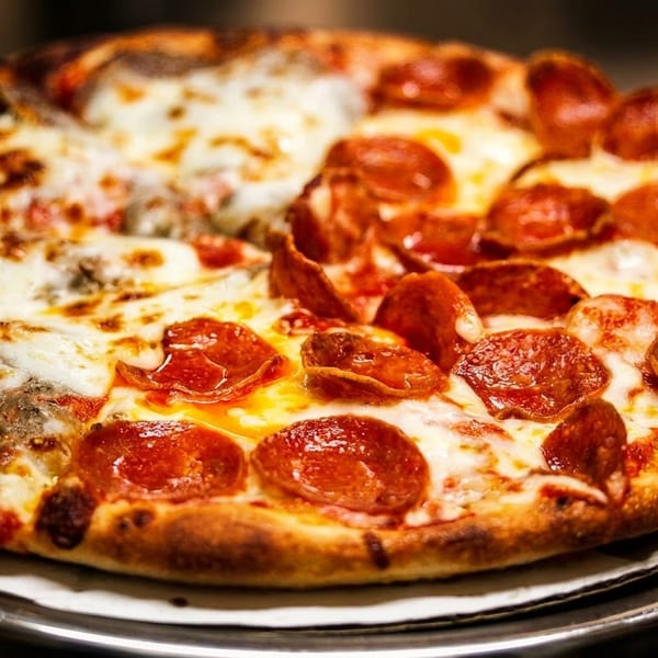 Half pepperoni and half sausage pizza with melted cheese on a metal stand.