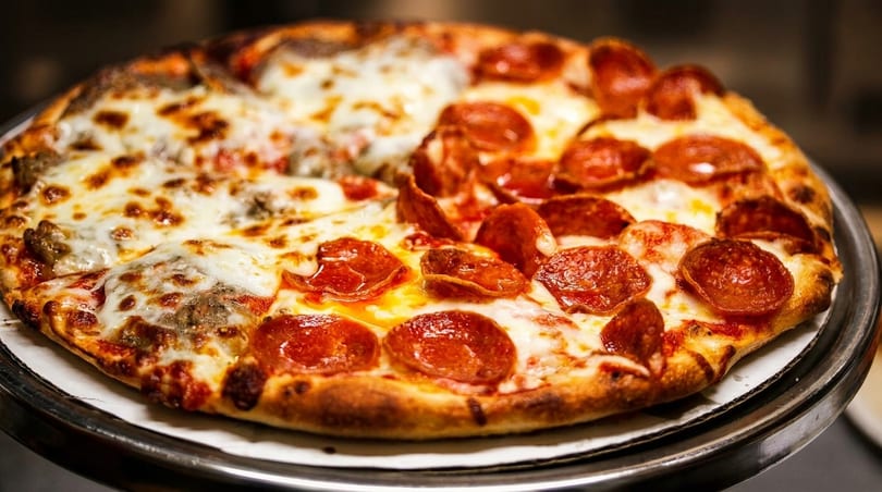 Half pepperoni and half sausage pizza with melted cheese on a metal stand.