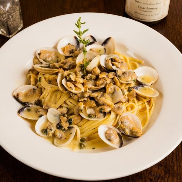 Linguine pasta with clams in a white wine sauce, garnished with a sprig of herb.