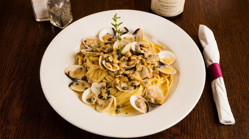 Linguine pasta with clams in a white wine sauce, garnished with a sprig of herb.