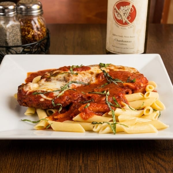 Chicken parmesan with penne pasta, tomato sauce, and basil, alongside a wine bottle and spices.